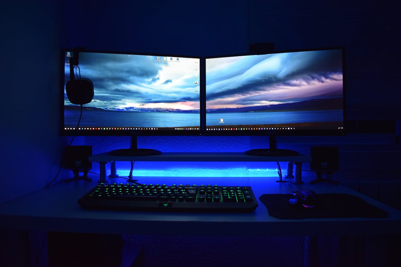 who-we-are Dual monitors with blue lighting on a gaming desk setup.
