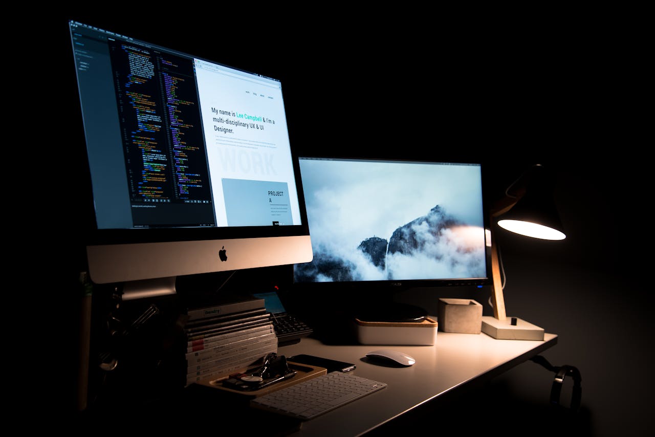 heros-img A clean and stylish workspace featuring dual monitors, a lamp, and office supplies.
